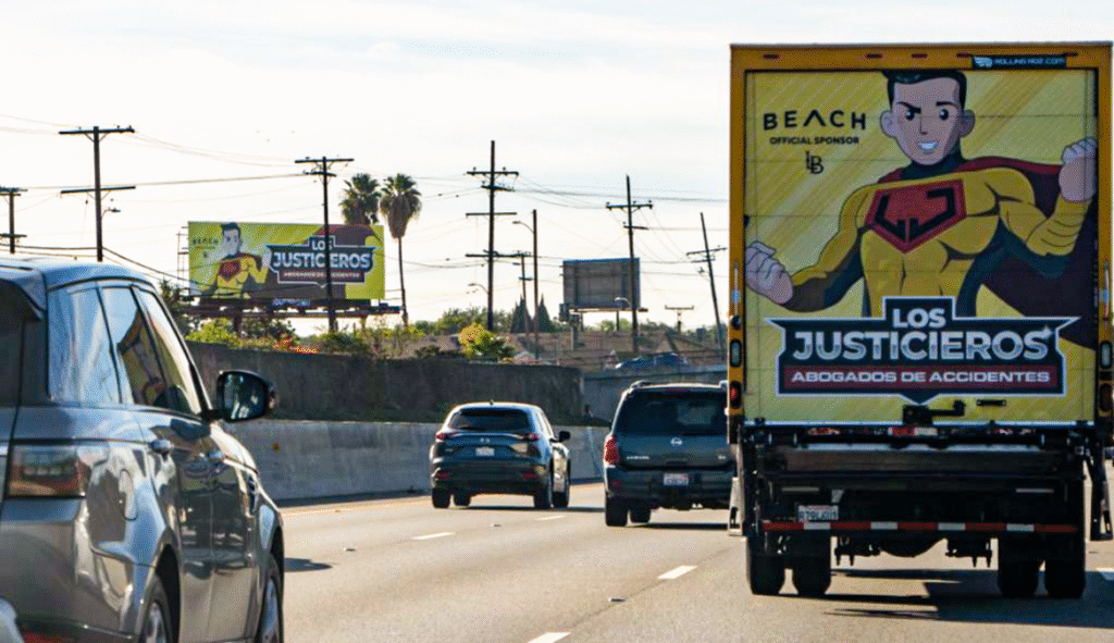 Image shows billboard advertising of Los Justicieros offering car and trucking accident injury legal services, with a truck also displaying the same advertising campaign in the foreground